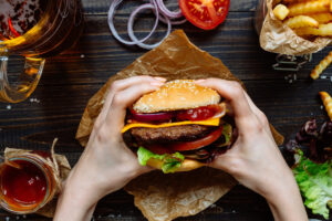 Hands holding fresh delicious burgers with french fries, sauce and beer on the wooden table top view.; Shutterstock ID 592466789